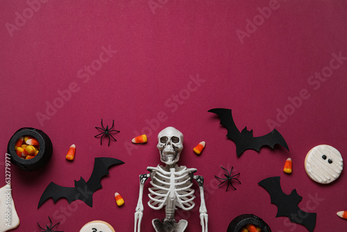 Composition with tasty candy corns, skeleton and Halloween decor on burgundy background