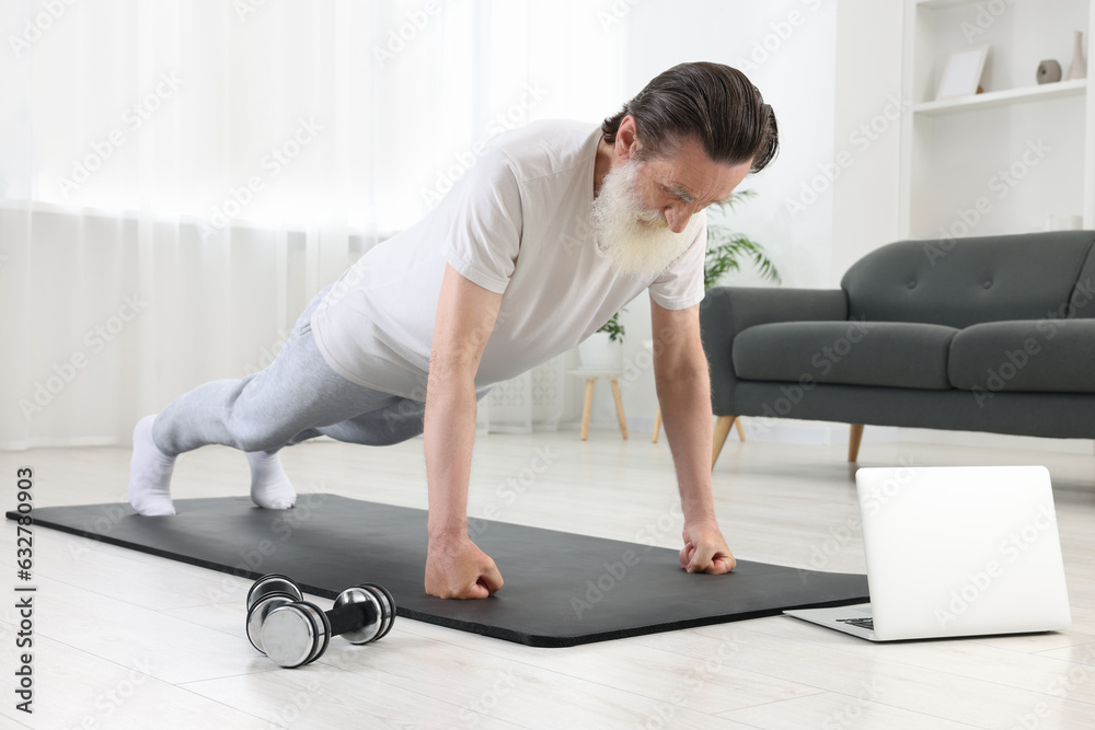 Fototapeta premium Senior man in sportswear doing exercises near laptop at home