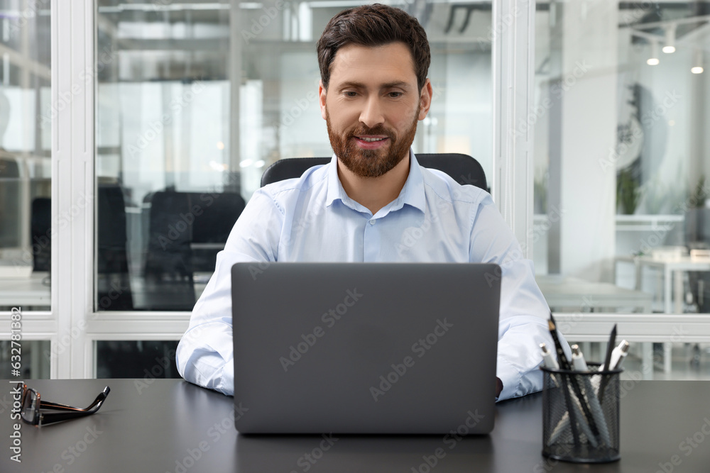 Man working on laptop at black desk in office Man working on laptop at black desk in office