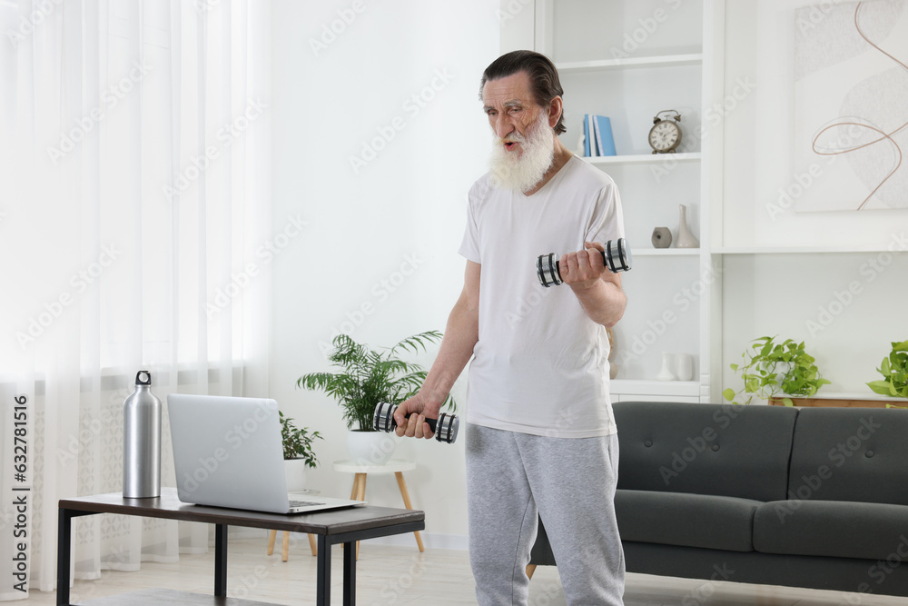 Senior man exercising with dumbbells while watching online tutorial at home. Sports equipment Senior man exercising with dumbbells while watching online tutorial at home. Sports equipment
