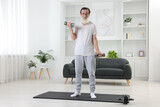 Senior man exercising with dumbbells on mat at home. Sports equipment
