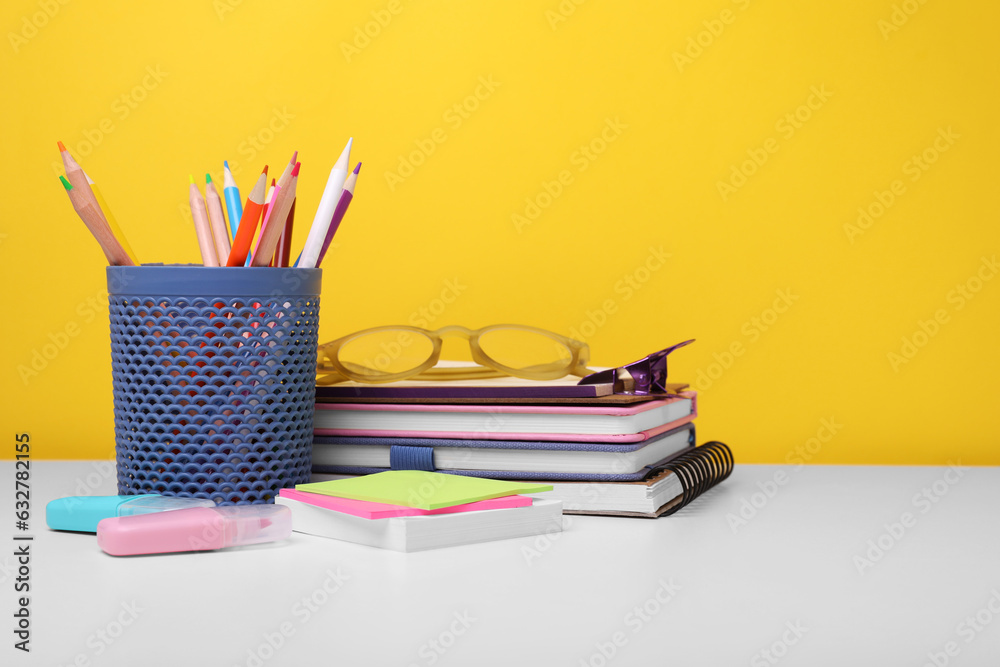 Fototapeta premium Different school stationery and glasses on white table against yellow background, space for text. Back to school