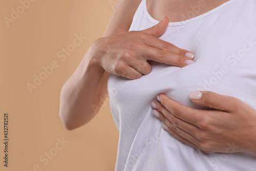 Woman doing breast self-examination on light brown background, closeup. Space for text photo