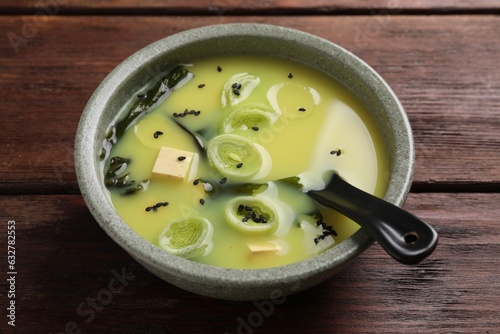 Bowl of delicious miso soup with tofu and spoon on wooden table, closeup