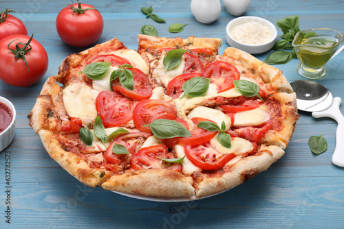 Delicious Caprese pizza and ingredients on blue wooden table, closeup