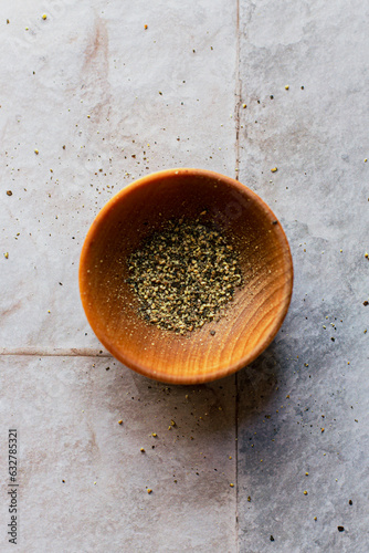 Flatlay of a small bowl of ground black pepper on a tiled surfacea photo