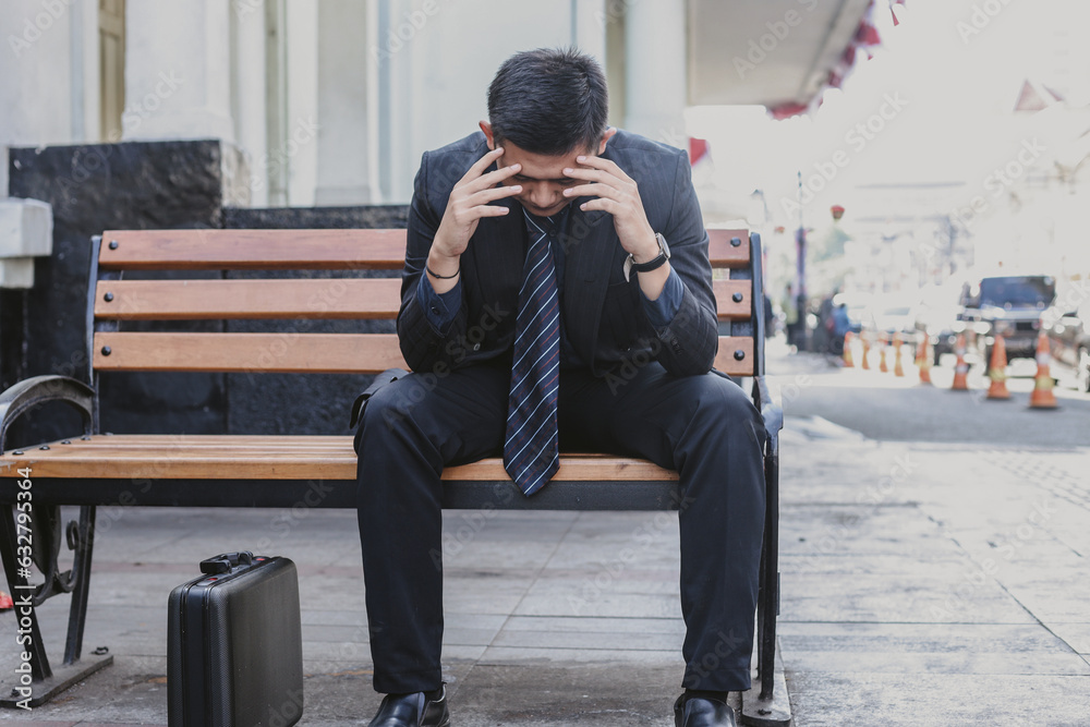 Sad failed young Asian businessman sitting alone on bench touching his head feeling despair Sad failed young Asian businessman sitting alone on bench touching his head feeling despair