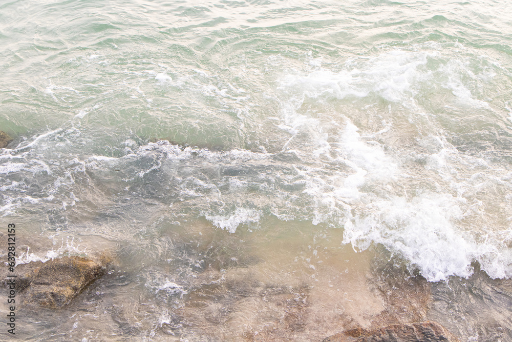 Obraz premium Water splashes from wave bumping against rocky shore brown. which is important tourist destination. Background image is sea blue of bright sunlight make picture very bright. Beach at Penang Malaysia.