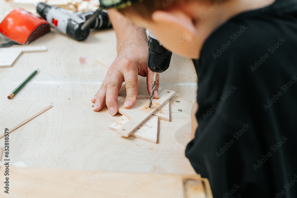 The process of learning carpentry, a close-up of a father and son working on wood, drilling a hole with a drill