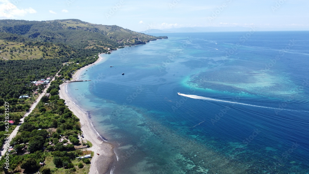 Scenic aerial view of Atauro Island in Timor-Leste with dive boat, coral reef, beautiful blue turquoise ocean water and rugged landscape of tropical island