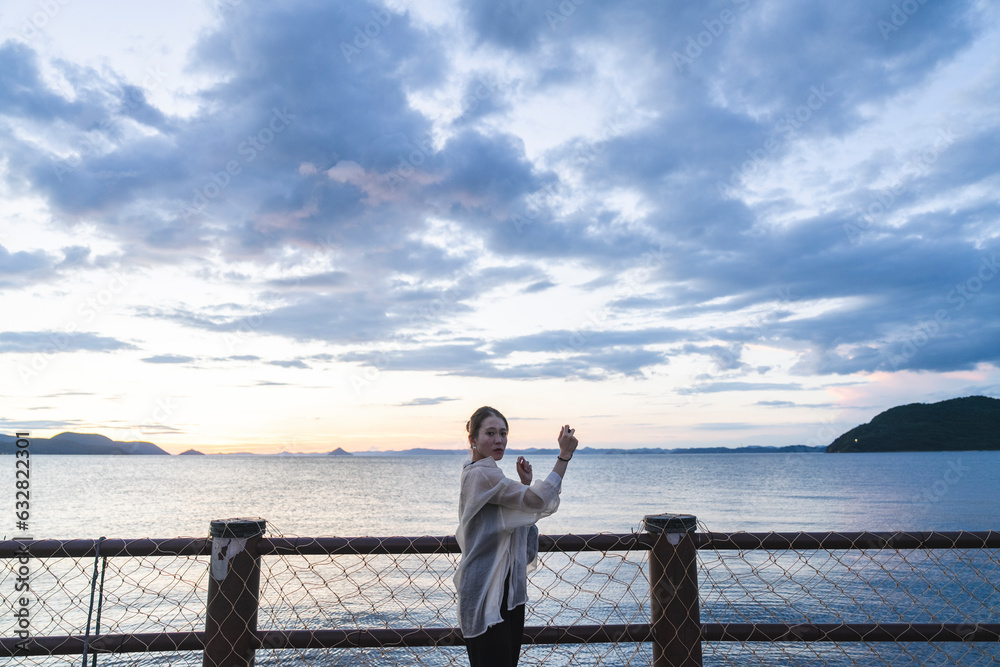 夕暮れの海で写真を撮る女性