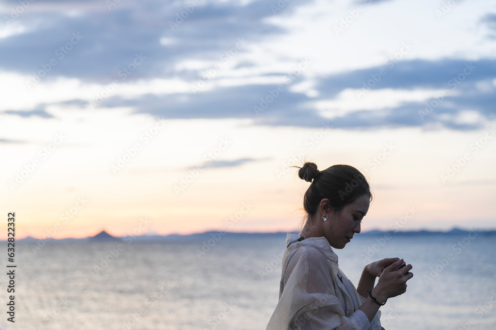 夕暮れの海で写真を撮る女性