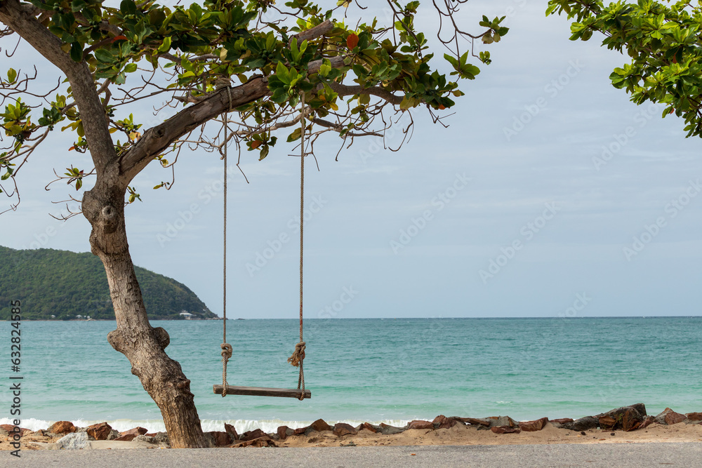 Wooden swing hanging under the trees by the sea There is a mountain in front on sunny day Wooden swing hanging under the trees by the sea There is a mountain in front on sunny day