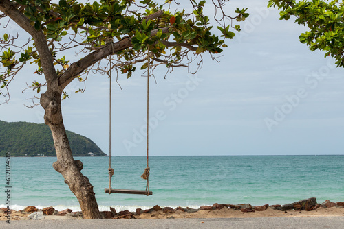 Wooden swing hanging under the trees by the sea There is a mountain in front on sunny day