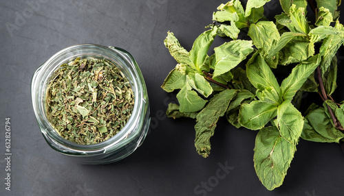 Dried peppermint in a glass jar and a bunch of fresh mint, medicine herb on black background, top view