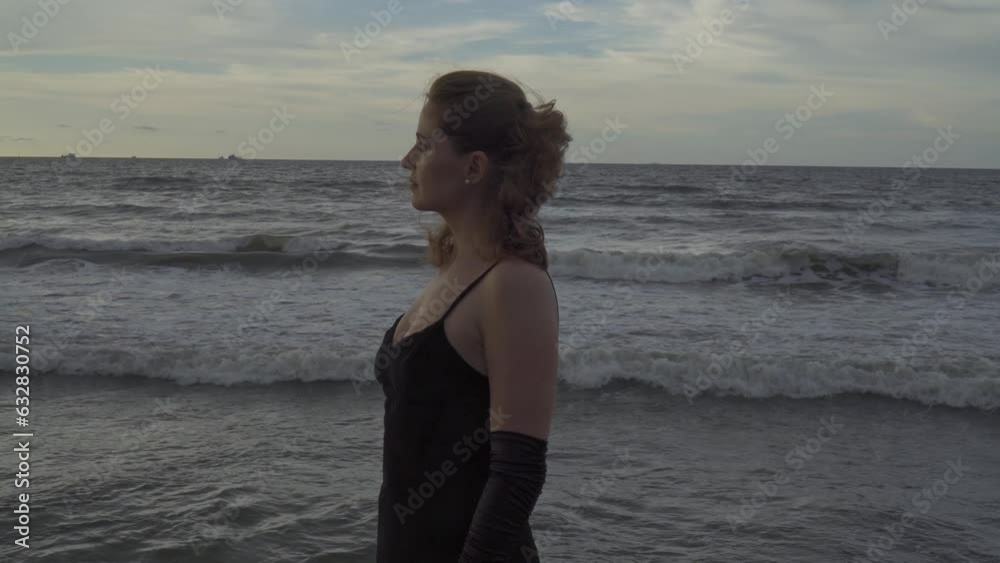 Model in a long black dress on the pier seaside posing over the cloudy sky Model in a long black dress on the pier seaside posing over the cloudy sky