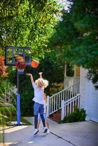 happy kids playing basketball at the driveway of their home. portable basketball hoop stand. active lifestyle. neighborhood activity sports