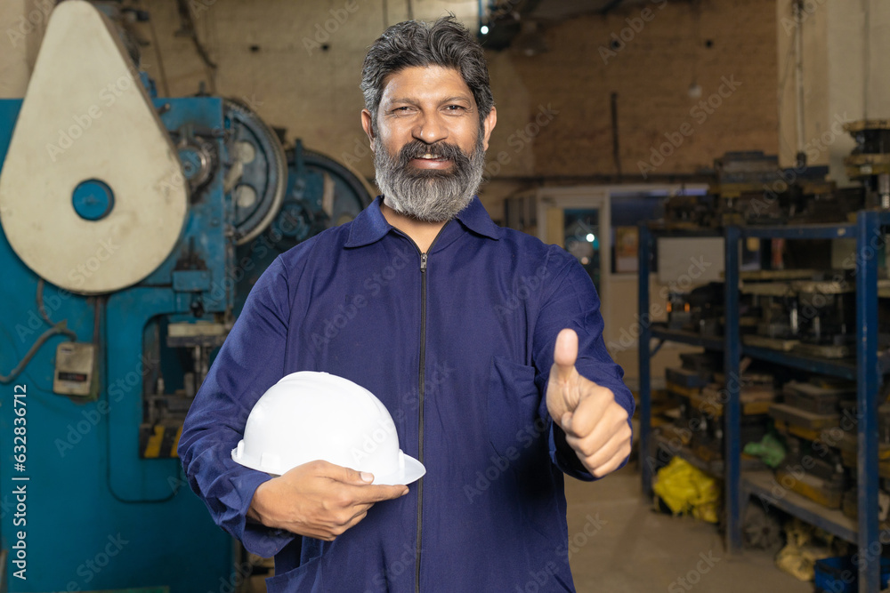 Indian worker,labor or technician standing and holding protective hard hat at factory Indian worker,labor or technician standing and holding protective hard hat at factory