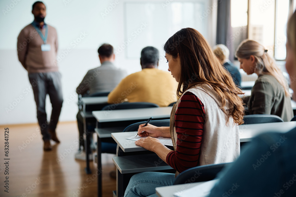 Rear view of woman writing an educational exam in classroom. Rear view of woman writing an educational exam in classroom.