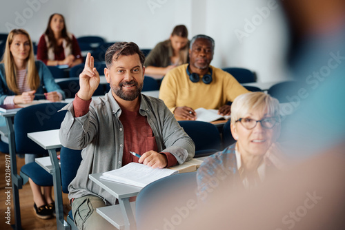 Mature man raising hand to ask question while attending class in lecture hall. photo
