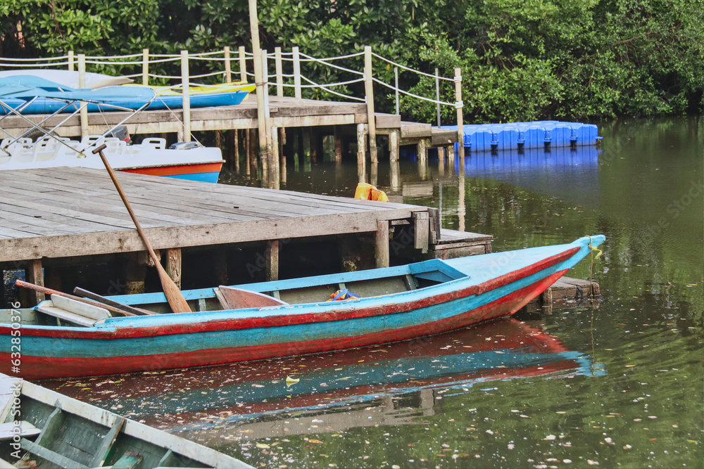 close up on a wooden boat beside a wooden pier ready for use with a background lake and trees.
