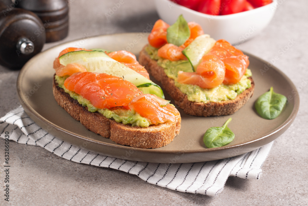 Two tasty open salmon sandwiches with avocado and cucumber. Morning healthy breakfast. Top view. Two tasty open salmon sandwiches with avocado and cucumber. Morning healthy breakfast. Top view.