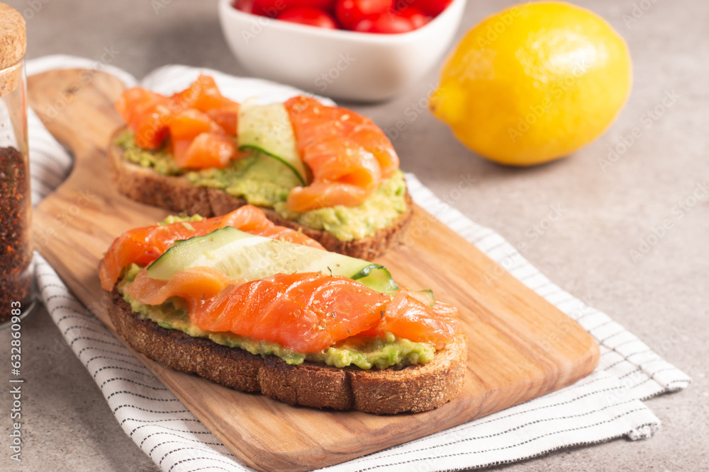 Two tasty open salmon sandwiches with avocado and cucumber. Morning healthy breakfast. Top view. Two tasty open salmon sandwiches with avocado and cucumber. Morning healthy breakfast. Top view.