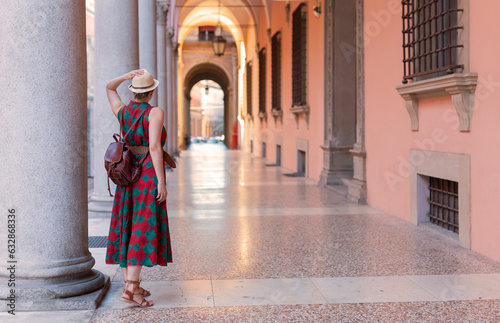 Young female tourist dressed casually standing with hat in the famous arched galleries in Bologna city in Italy. Bologna is student city and home to the oldest university in the world photo