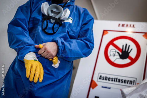 Mann säubert Gebäude von Asbest im blauen Schutzanzug mit gelben Handschuhen und einer Schutzmaske  photo