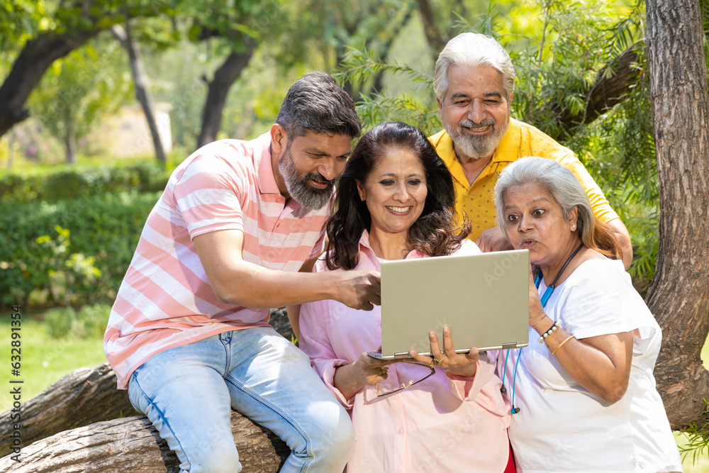 Indian man showing to his family how to use laptop at park Indian man showing to his family how to use laptop at park