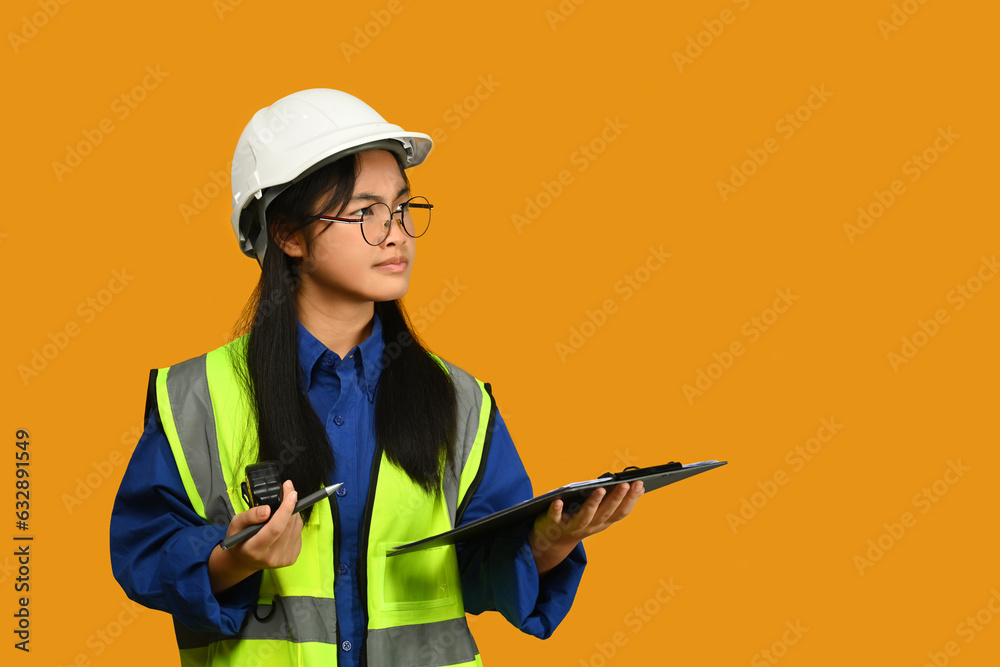 Asian girl wearing helmet and vest isolated on yellow background, future dream job career as engineer and architect Asian girl wearing helmet and vest isolated on yellow background, future dream job career as engineer and architect