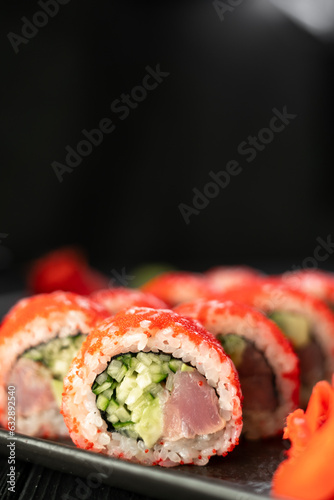 Delicious sushi roll california with tuna cucumber cheese and masago caviar on top on a stone plate on black background. Vertical banner.