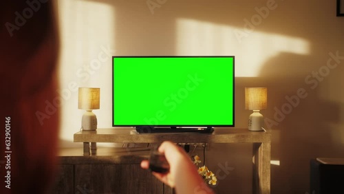 Woman watching TV with green screen in living room. Female person switching channels, using remote control, sitting on sofa.