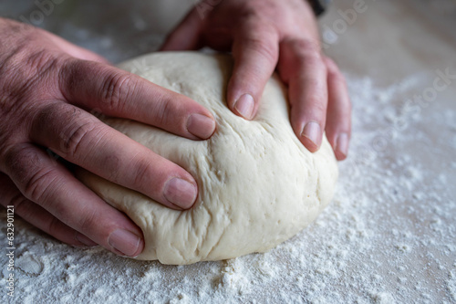 Male hands kneading a yeast dough on kitchen counter with flour
