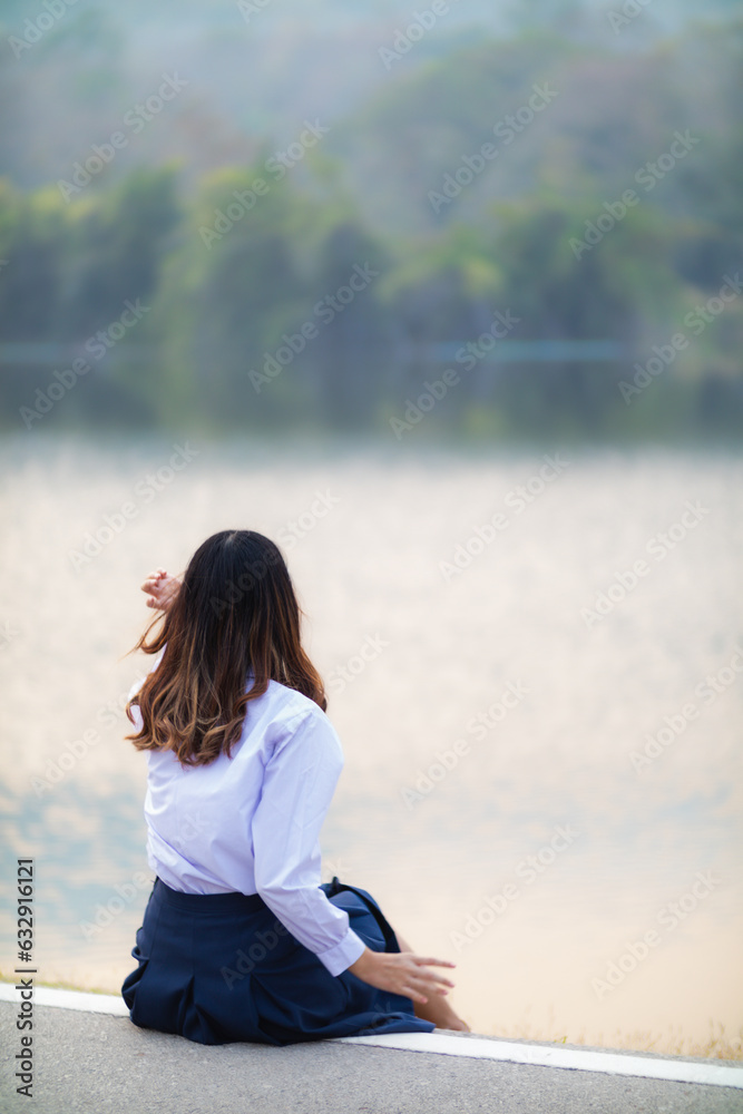 young woman sits on walkway by reservoir watching beautiful scenery of reservoir alone in the evening. back of woman sitting by reservoir alone in evening and with copy space for text.