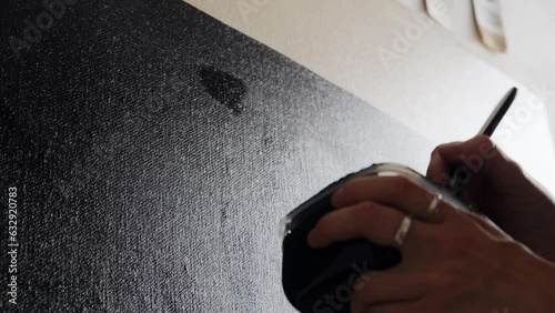 Slow application of black color paint on the canvas close-up. The movement of the brush by the artist's hand on a blank canvas. Fine art, abstract painting, creative process.