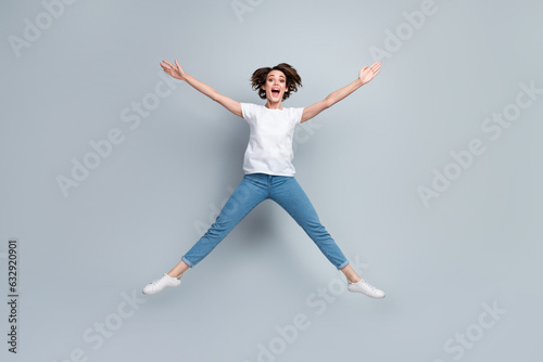Full size photo of astonished ecstatic girl dressed white t-shirt jeans jumping like star hands up isolated on gray color background © deagreez