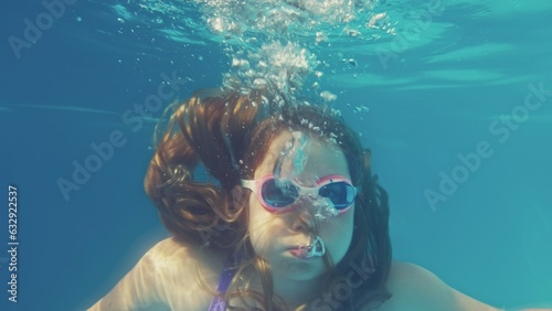 Young Caucasian Girl Diving in Swimming Pool Breathing Out Air Bubbles