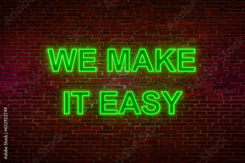 Brick wall at night with the text "We make it easy" in green neon letters. Easy going, positive emotion, never mind, relaxation, motto, slogan, cool attitude. 3D illustration