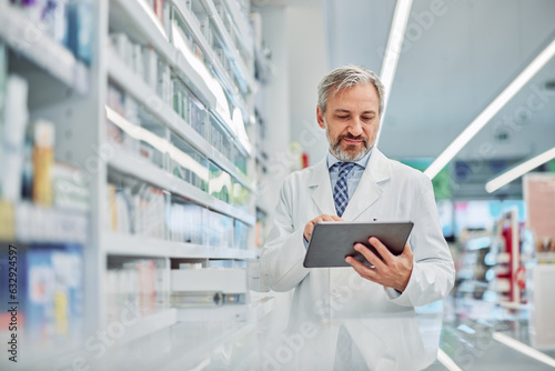 A senior male pharmacist holding a digital tablet and using it for work. photo