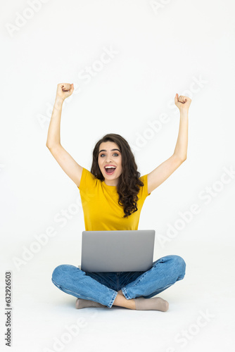 Excited happy pretty woman raised hands, working with laptop, sitting with crossed legs on the white floor © F8  \ Suport Ukraine
