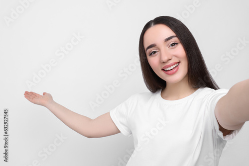 Smiling young woman taking selfie on white background