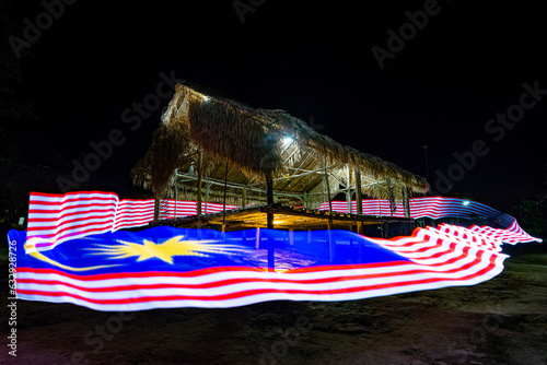 A traditional hut aglow under the cover of night, adorned with resplendent LED lights forming the luminous tapestry of Malaysia's national flag at Royal Belum National Rainforest Park of Malaysia.