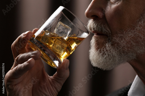 Senior man drinking whiskey on brown background, closeup
