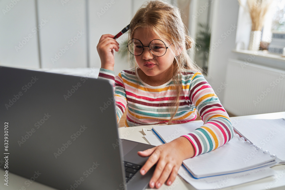 Caucasian elementary age girl studying on laptop and having problems with understanding Caucasian elementary age girl studying on laptop and having problems with understanding