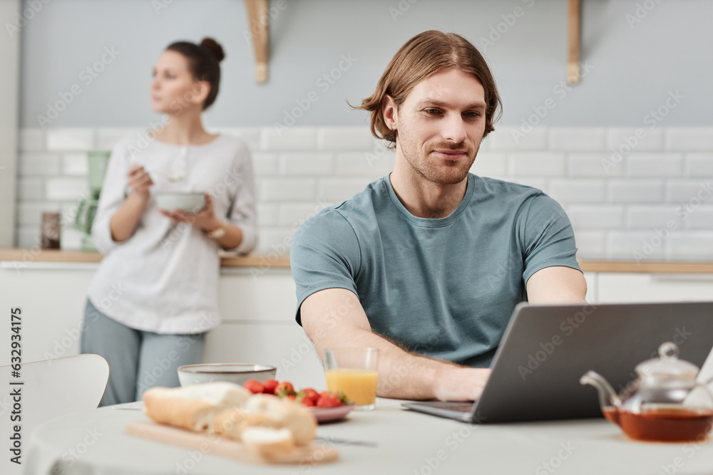 Portrait of smiling young man using laptop in kitchen during breakfast, copy space Portrait of smiling young man using laptop in kitchen during breakfast, copy space