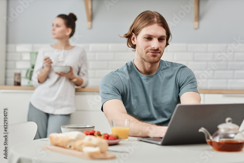 Portrait of smiling young man using laptop in kitchen during breakfast, copy space