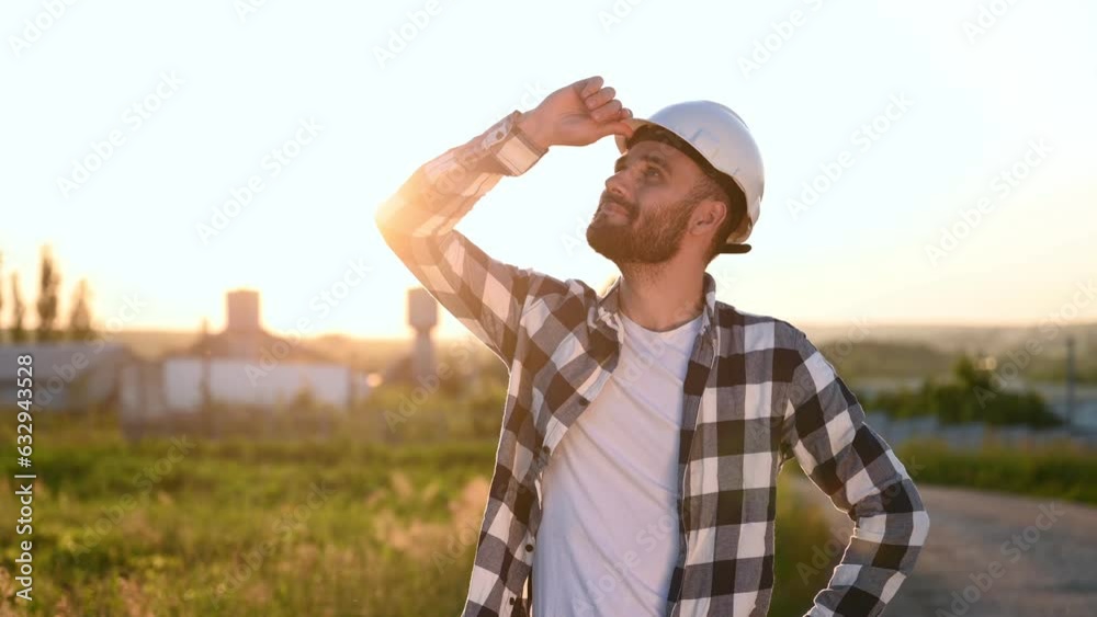 Looks up, then smiling. Service engineer is on the field with windmills. Looks up, then smiling. Service engineer is on the field with windmills.