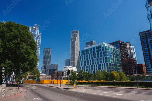 Empty road by modern buildings in capital city. Highway surrounded by trees with clear blue sky in background. View of downtown district during sunny day. © Aerial Film Studio