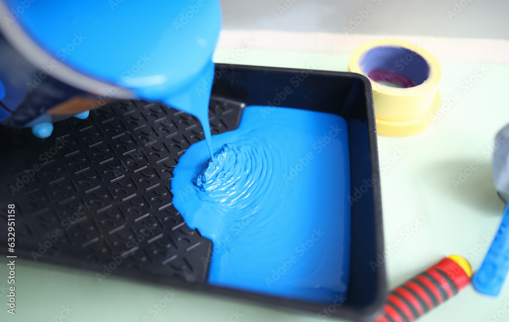 Hand pour blue paint from can into black plastic tray. In background there are two masking tape of different width. Hand pour blue paint from can into black plastic tray. In background there are two masking tape of different width.